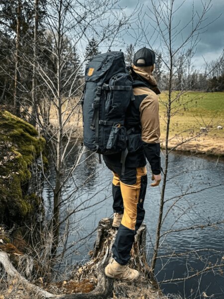 Outdoorowe spodnie Fjällräven i plecak nad brzegiem rzeki w przyrodzie. Foto: Rigad