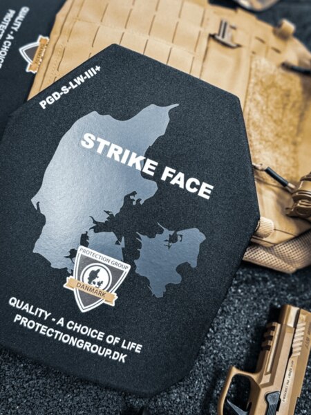 Twardy balistyczny panel ze stroną STRIKE FACE (PGD); w tle plate carrier i służbowy pistolet, szczegóły przed włożeniem do nosidła.