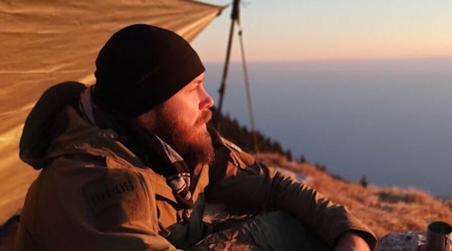 Mężczyzna siedzi o zachodzie słońca i ma na sobie zimową czapkę Contact Fleece Beanie marki Snugpak