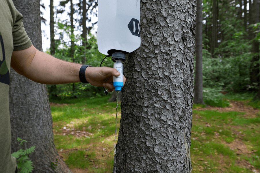 Gravitacyjny filtr wody zawieszony na drzewie podczas filtracji wody na łonie natury. Foto: Rigad