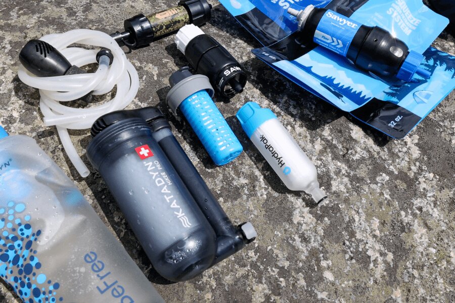 Zestaw różnych przenośnych filtrów wodnych Sawyer, HydraPak i Katadyn na kamiennym podłożu. Foto: Rigad