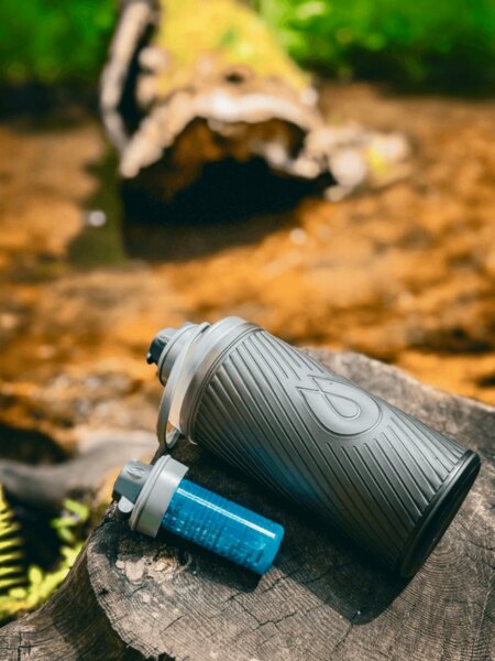 Butelka Flux HydraPak z filtrem Cap położona na pniu w naturze, idealna na podróże i aktywność outdoorową. Foto: Rigad