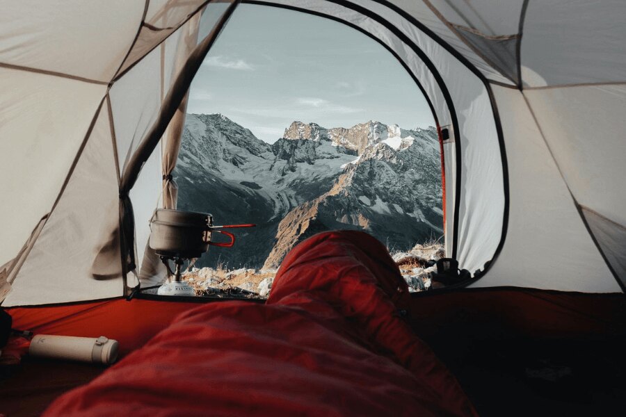 Widok z czerwonego śpiwora na ośnieżone góry. Źródło: https://www.pexels.com/cs-cz/foto/krajina-hory-cestovani-dobrodruzstvi-9166687/