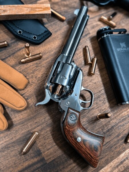 Rewolwer Ruger z długą lufą i drewnianą rękojeścią pomiędzy nabojami a sprzętem outdoorowym.