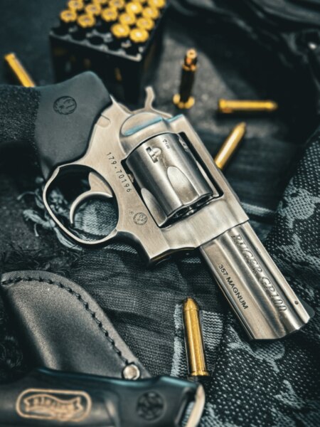 Rewolwer Ruger GP100 w kalibrze .357 Magnum położony obok naboi i kabury strzeleckiej.