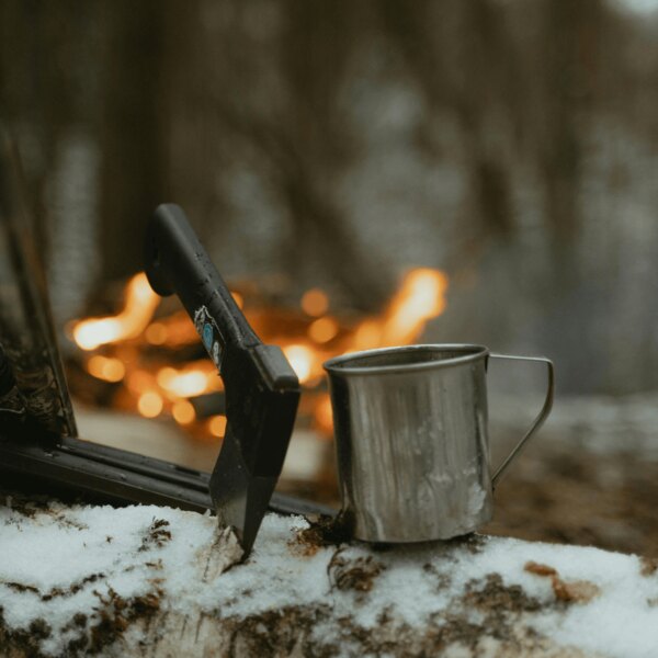 Siekiera bushcraftowa i metalowy kubek w lesie przy ogniu. Źródło: https://www.pexels.com/cs-cz/foto/ryma-studeny-snih-priroda-6204650/
