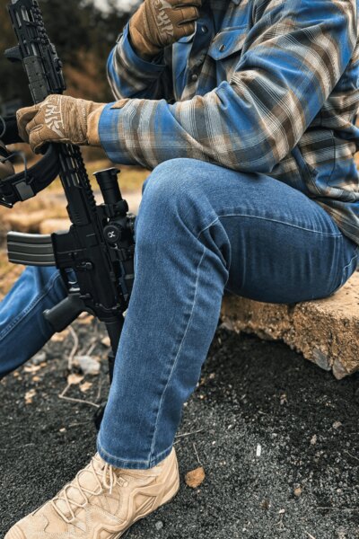 Mężczyzna w spodniach Treadstone Jeans<sup>&reg;</sup> Helikon-Tex<sup>&reg;</sup> w koszuli w kratę z karabinem. Foto: Rigad