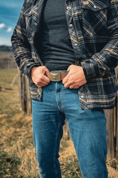 Mężczyzna w spodniach Treadstone Jeans<sup>&reg;</sup> Helikon-Tex<sup>&reg;</sup> w koszuli w kratę trzyma się za pasek. Foto: Rigad
