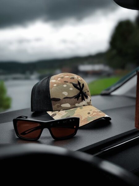 Czapka trucker Multicam z logo Unity Tactical i ochronne okulary strzeleckie na desce rozdzielczej. Foto: Rigad