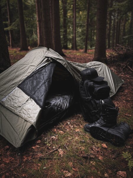 Biwakowy worek Snugpak z rozłożonym śpiworem, obok niego plecak i zimowe buty, przygotowane do awaryjnego noclegu na łonie natury. Foto: Rigad