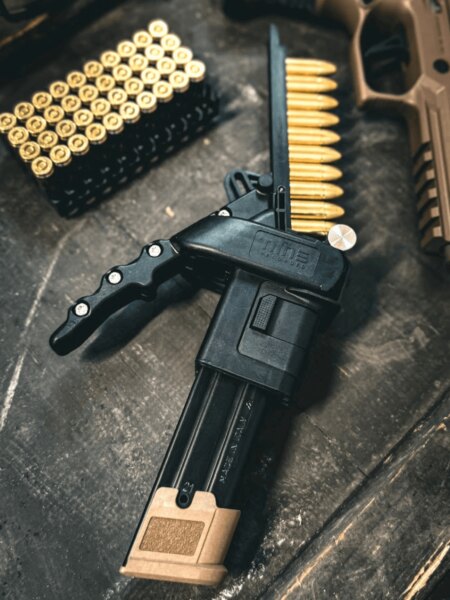 Ładowarka magazynków Nine Reloaded obok nabojów kalibru 9 mm Luger i pistoletu.