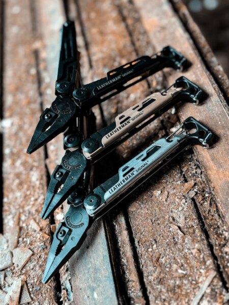 Trzy multitooly Leatherman Signal w różnych kolorach położone na drewnianej powierzchni.