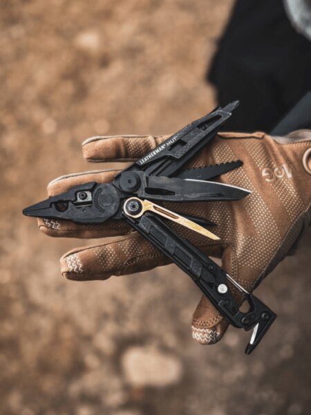 Multitool Leatherman MUT rozłożony na dłoni w taktycznej rękawicy.