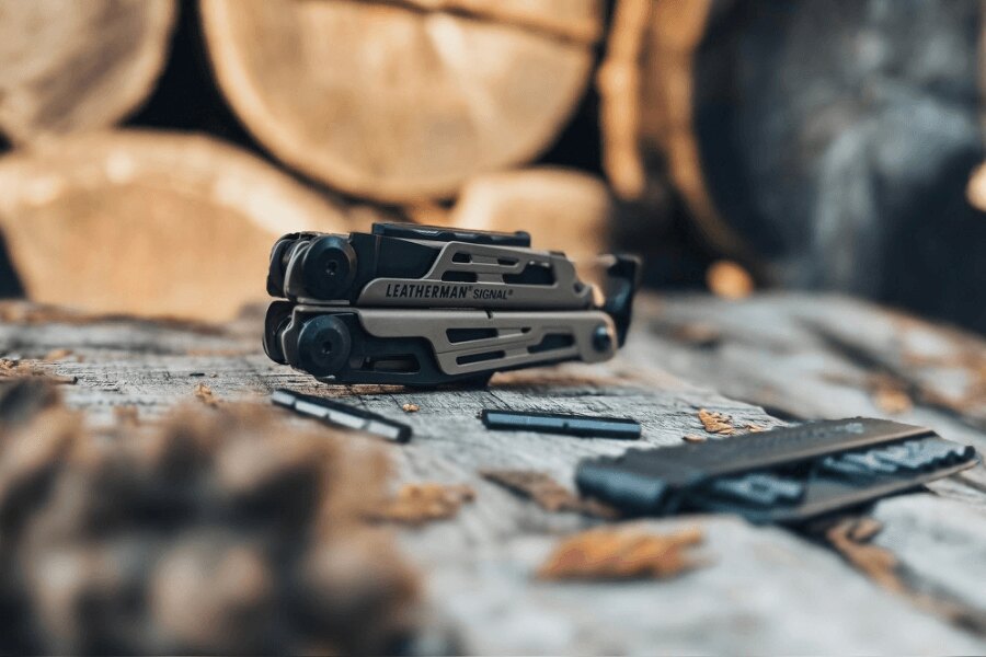 Leatherman Signal umieszczony na drewnianym stole z bitami i akcesoriami w środowisku outdoorowym.