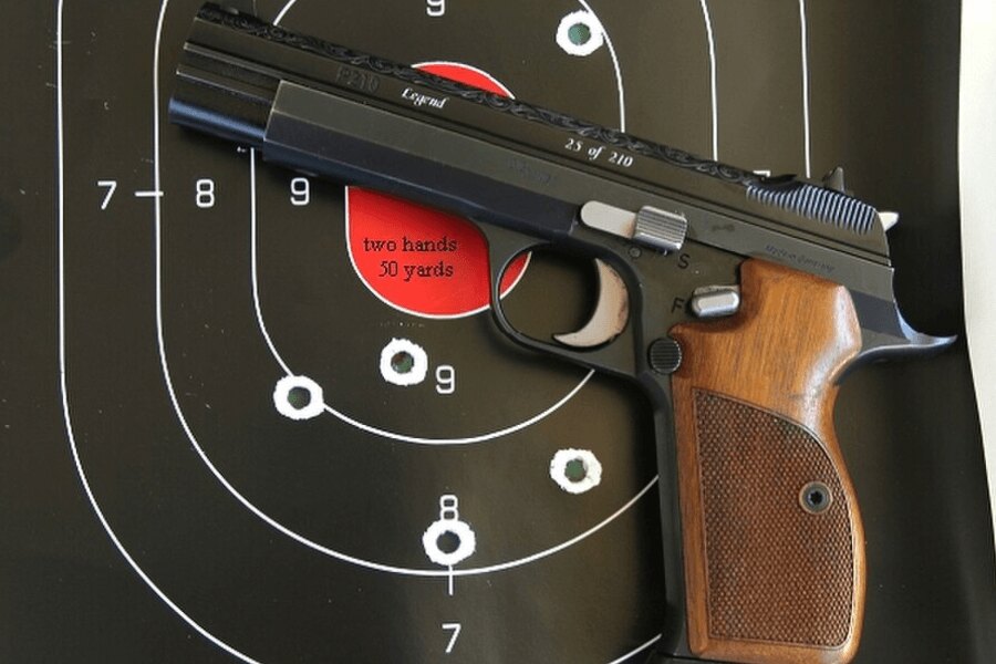 Pistolet SIG P210 położony przed tarczą strzelniczą.