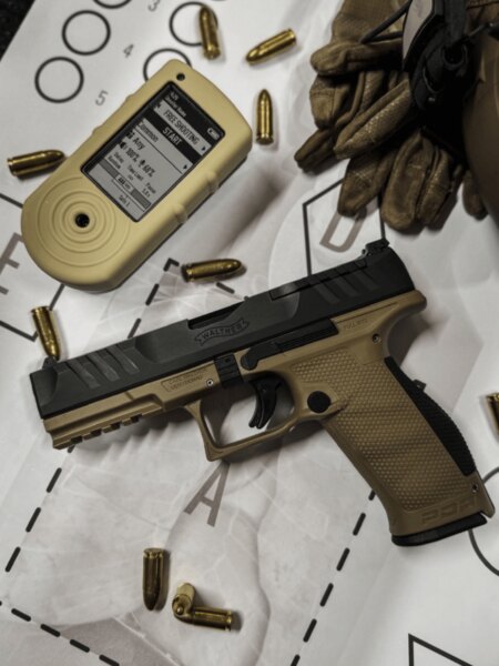 Pistolet Walther PDP Full Size z zegarem strzeleckim, nabojami i rękawicami położony na tarczy.