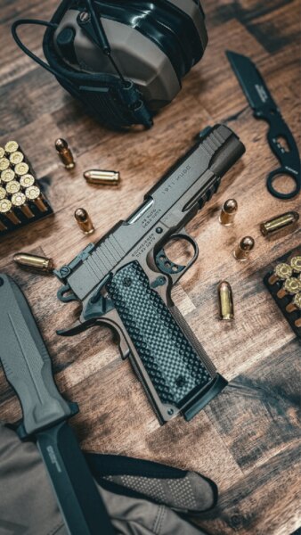 Pistolet Schmeisser HUGO 1911 5" w kalibrze .45 ACP położony na stole z amunicją i sprzętem strzeleckim.