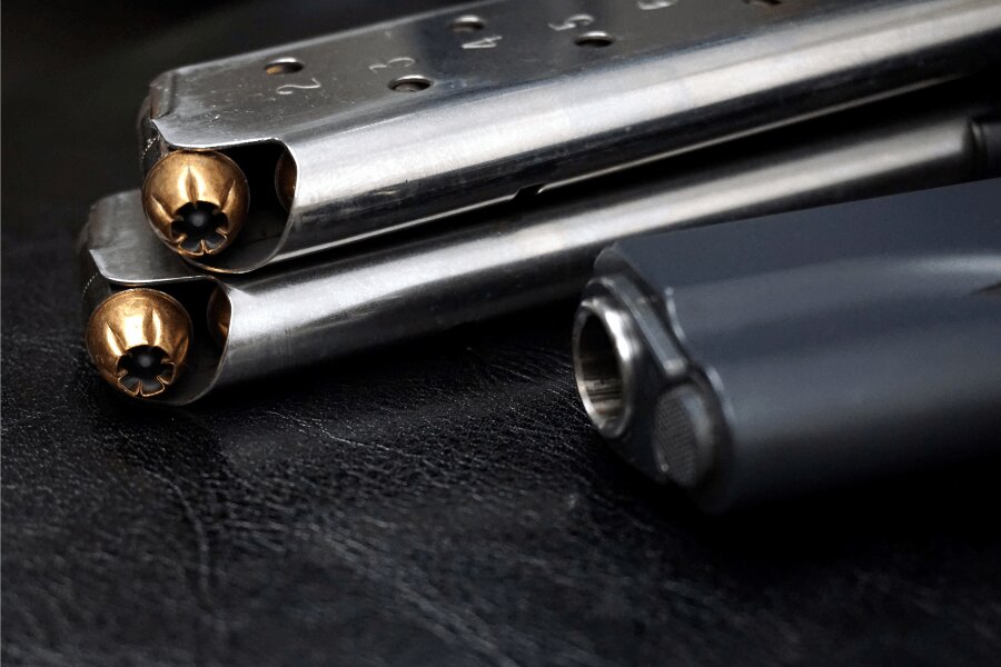 Szczegół magazynków do pistoletu M1911 z nabojami .45 ACP i części pistoletu w tle.
