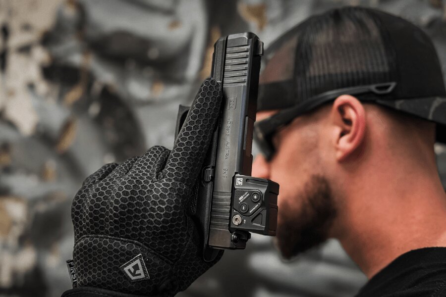 Szczegóły pistoletu Glock 45 z kolimatorem trzymane w rękawicy.